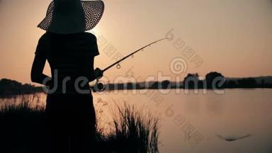 戴着帽子的年轻女人的剪影，在黎明时分用鱼竿捕鱼